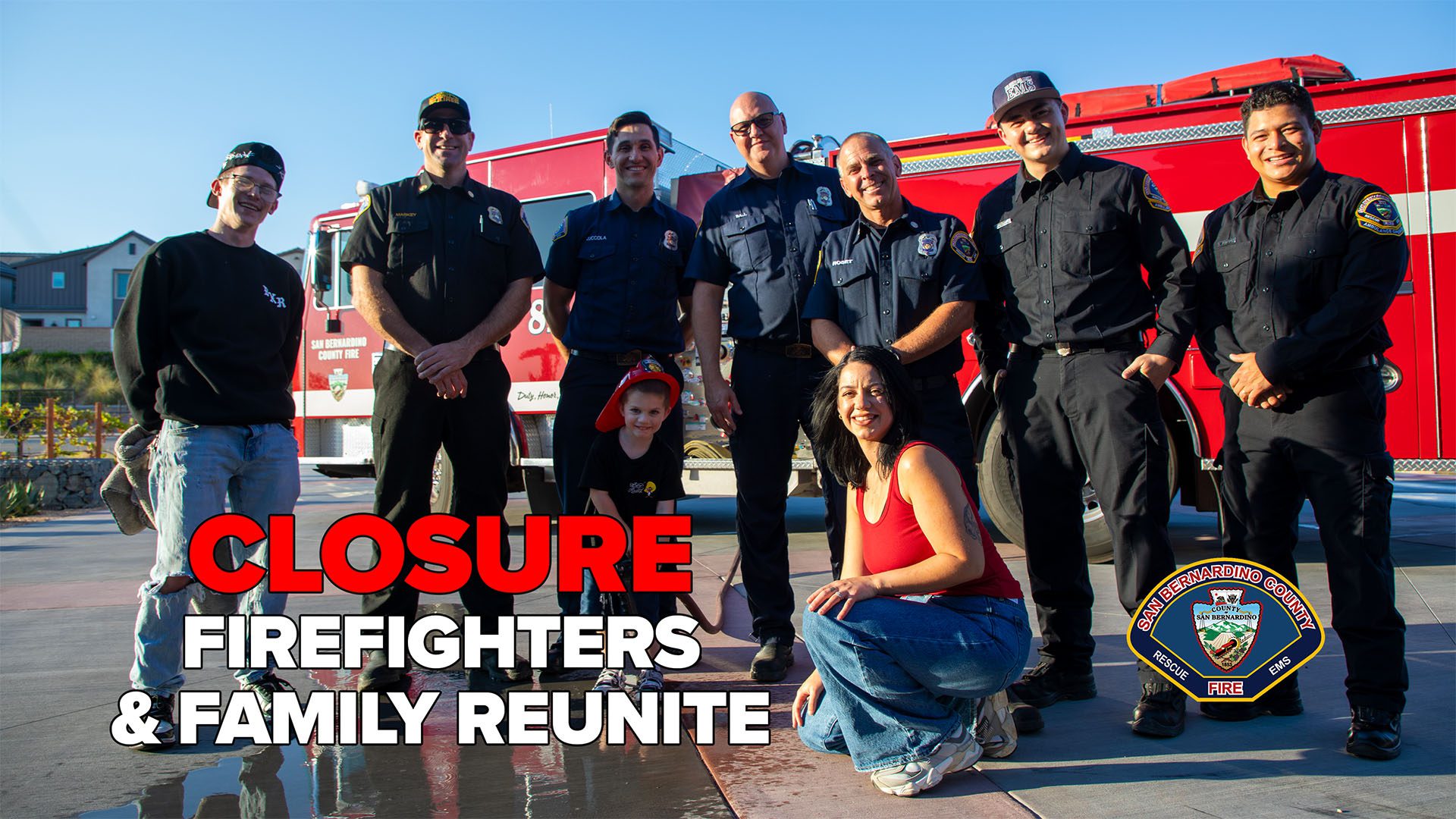 A group of San Bernardino County firefighters in uniform stand smiling in front of a red fire engine, posing with a family including a man, a woman kneeling in front, and a young child wearing a firefighter helmet. Bold text on the left reads “Closure: Firefighters & Family Reunite.” The San Bernardino County Fire Department badge logo is displayed in the lower right corner.