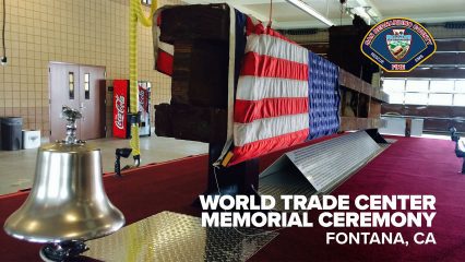 A steel beam from the World Trade Center, draped with an American flag, is displayed indoors on a stand. A silver ceremonial bell sits in the foreground on a metal platform. The display rests on a red carpet with an informational plaque beneath the beam. Text on the image reads, “World Trade Center Memorial Ceremony, Fontana, CA,” alongside the San Bernardino County Fire Department logo.