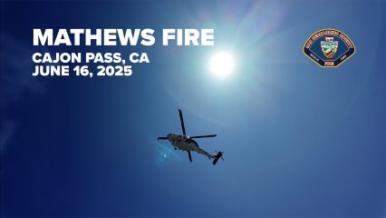A firefighting helicopter flies overhead against a clear blue sky with the sun shining brightly near the top right corner. Bold white text on the left reads “MATHEWS FIRE, CAJON PASS, CA, JUNE 16, 2025.” In the upper right corner, the San Bernardino County Fire Department emblem is displayed.