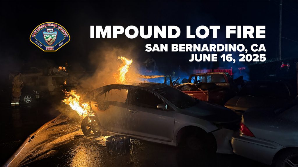 A nighttime scene of a fire at an impound lot in San Bernardino, California, on June 16, 2025. The image shows a white sedan engulfed in flames, particularly around the front left wheel and roof area, with fire spreading to other nearby vehicles. A firefighter is faintly visible on the left side of the image. In the background, blue smoke and emergency lights illuminate the area. The logo of the San Bernardino County Fire Department appears in the top left corner, and bold white text across the top reads: “IMPOUND LOT FIRE – SAN BERNARDINO, CA – JUNE 16, 2025.”