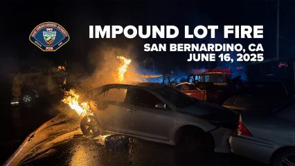 A nighttime scene of a fire at an impound lot in San Bernardino, California, on June 16, 2025. The image shows a white sedan engulfed in flames, particularly around the front left wheel and roof area, with fire spreading to other nearby vehicles. A firefighter is faintly visible on the left side of the image. In the background, blue smoke and emergency lights illuminate the area. The logo of the San Bernardino County Fire Department appears in the top left corner, and bold white text across the top reads: “IMPOUND LOT FIRE – SAN BERNARDINO, CA – JUNE 16, 2025.”