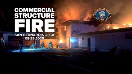Firefighters work to control a large commercial structure fire at night in San Bernardino, California. Flames and heavy smoke rise from the roof of a two-story building as crews prepare hoses. Text overlay reads “Commercial Structure Fire, San Bernardino, CA, 08-22-2025” with the San Bernardino County Fire Department logo.