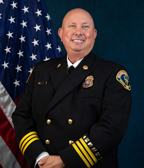 Division Chief Mike O’Bier of San Bernardino County Fire stands in uniform smiling in front of the American flag.