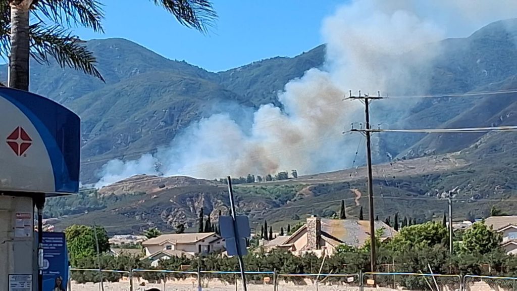 Smoke rising in the background in the hills with mountains behind it at a gas station