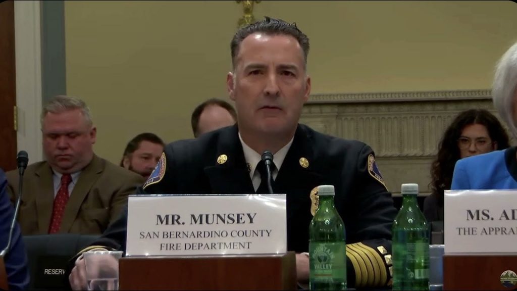 San Bernardino County Fire Department Chief sitting at wood table with folded name tag speaking to Congress with people in the background